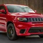 A red 2020 Jeep Grand Cherokee Trackhawk is shown driving on an empty road after leaving a Certified Pre-Owned Jeep dealership.