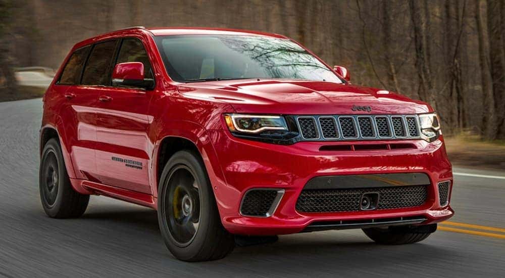 A red 2020 Jeep Grand Cherokee Trackhawk is shown driving on an empty road after leaving a Certified Pre-Owned Jeep dealership.