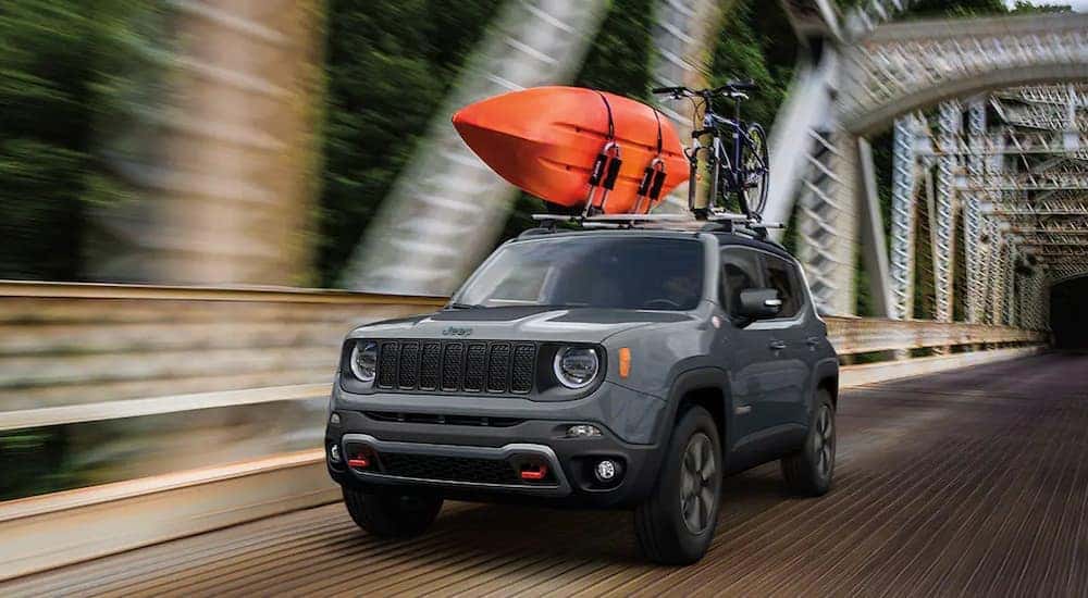 A grey 2020 Jeep Renegade Trailhawk is shown with a kayak on the roof while driving on a bridge.