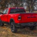 A red 2022 Ram 1500 Rebel is shown from a rear angle driving on a grassy trail.