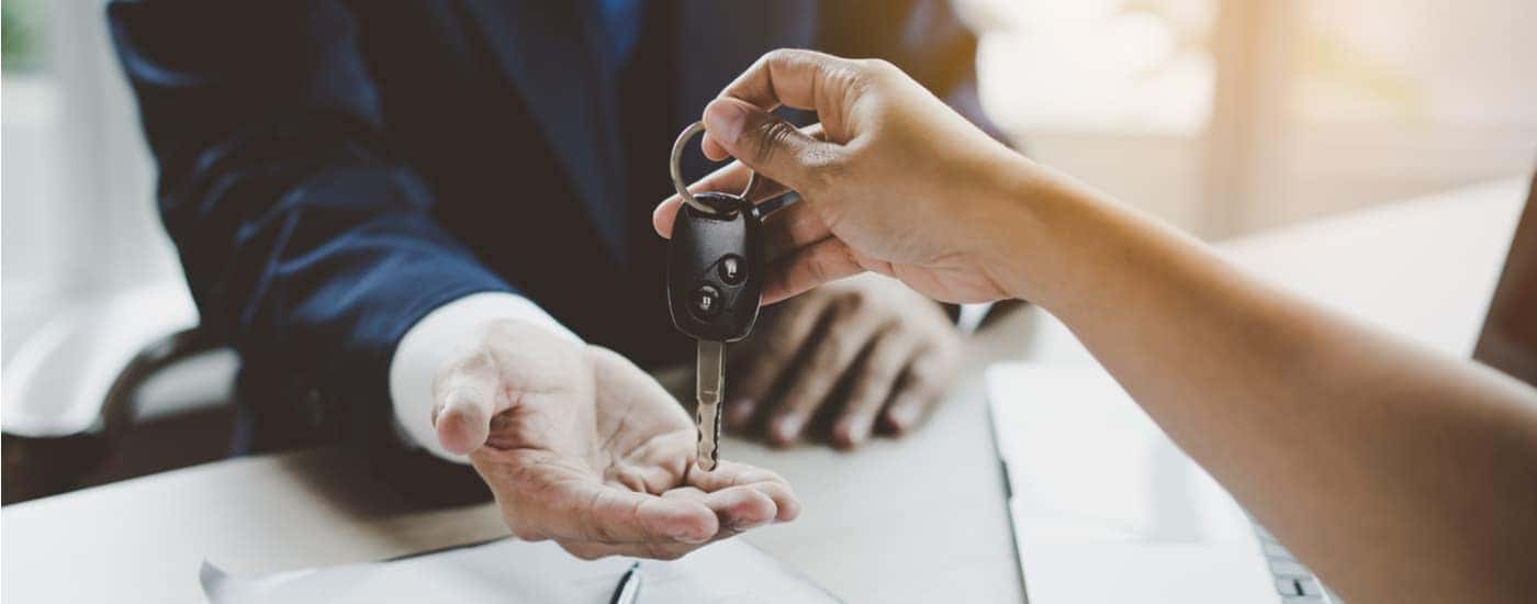 A person is shown handing a salesman a car key after selling their car.