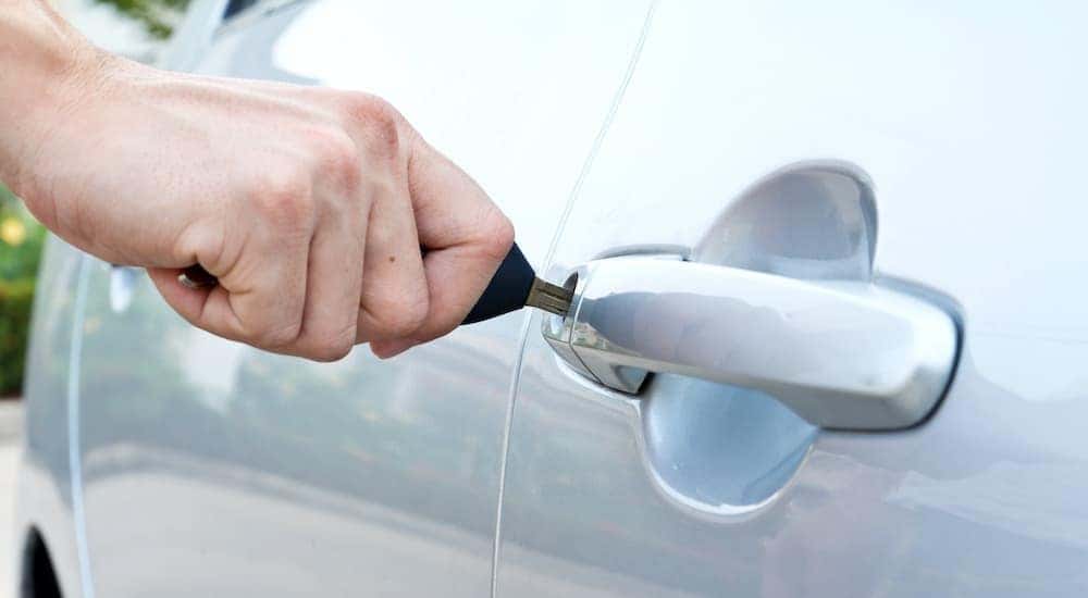 A close up shows a person unlocking a car door.