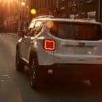 A white 2021 Jeep Renegade is shown from behind driving through a city at dusk.