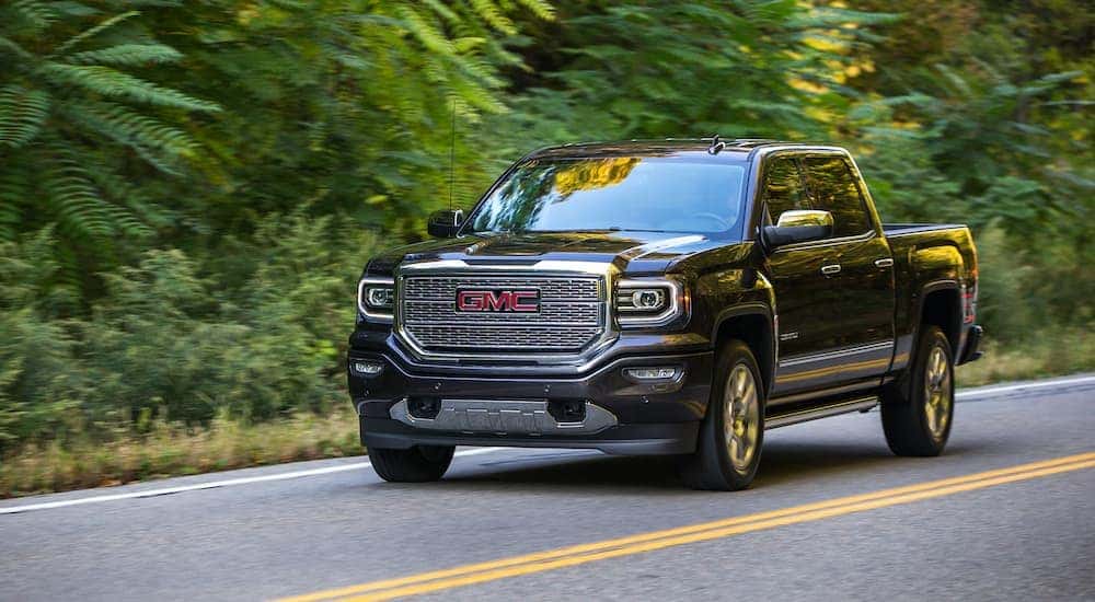 A black 2016 GMC Sierra 1500 Denali is shown driving down a wooded road.