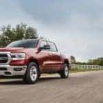 A red 2020 Ram 1500 is shown driving past a white fence after visiting a used work truck dealer.