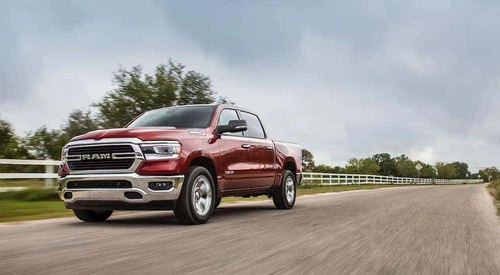 A red 2020 Ram 1500 is shown driving past a white fence after visiting a used work truck dealer.