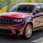 A red 2018 Jeep Grand Cherokee is shown from the front driving on an open road.