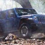 A blue 2020 Jeep Wrangler Unlimted is shown from the side parked in a forest.