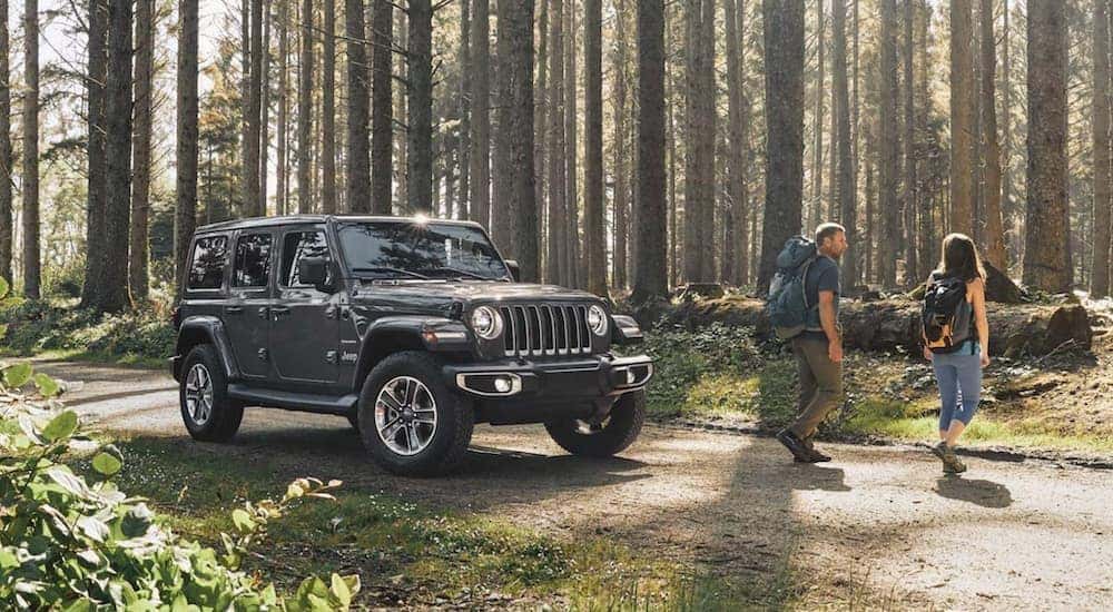 A grey 2020 Jeep Wrangler Unlimited is shown parked on a dirt road as two hikers walk by.