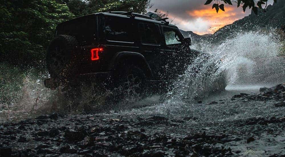 A popular used Jeep Wrangler, a black 2020 Jeep Wrangler is shown from the side driving through a river.