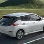 A white 2021 Nissan LEAF is shown from the side driving on an open road.