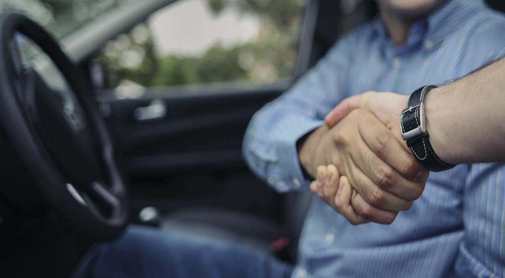 A person is shown shaking hands with a salesman after searching "used cars for sale."
