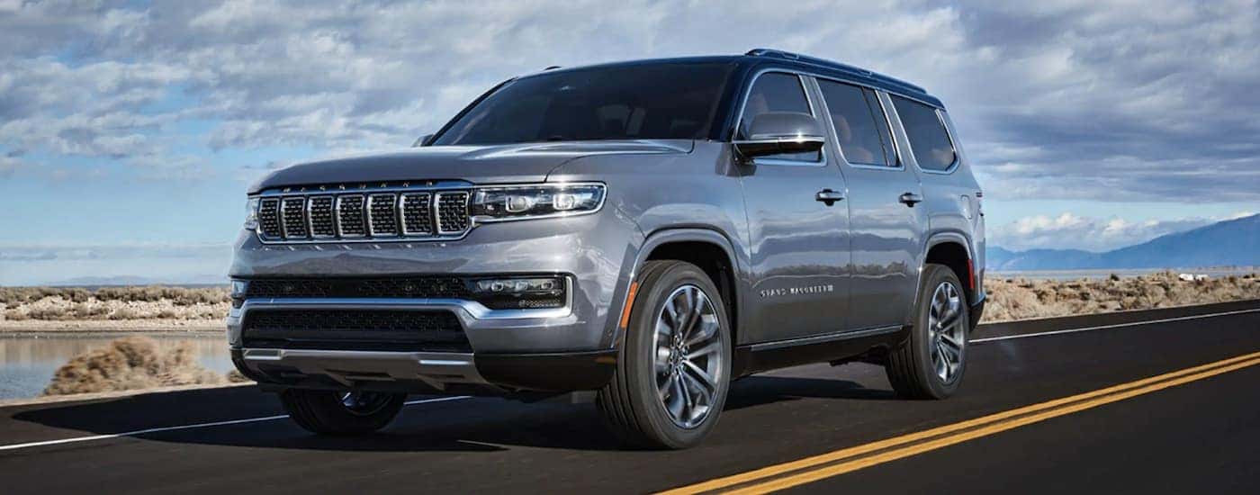 A grey 2022 Grand Wagoneer is shown from the front driving on an open road after leaving a Grand Wagoneer dealership.