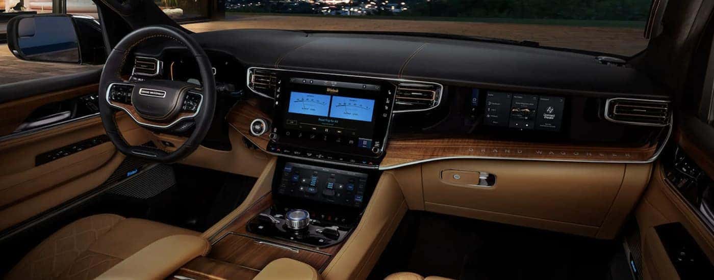 The black and tan interior of a 2022 Grand Wagoneer shows the steering wheel and infotainment screen.