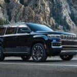 A black 2022 Grand Wagoneer is shown from the side driving on an open road after leaving a Grand Wagoneer dealership.