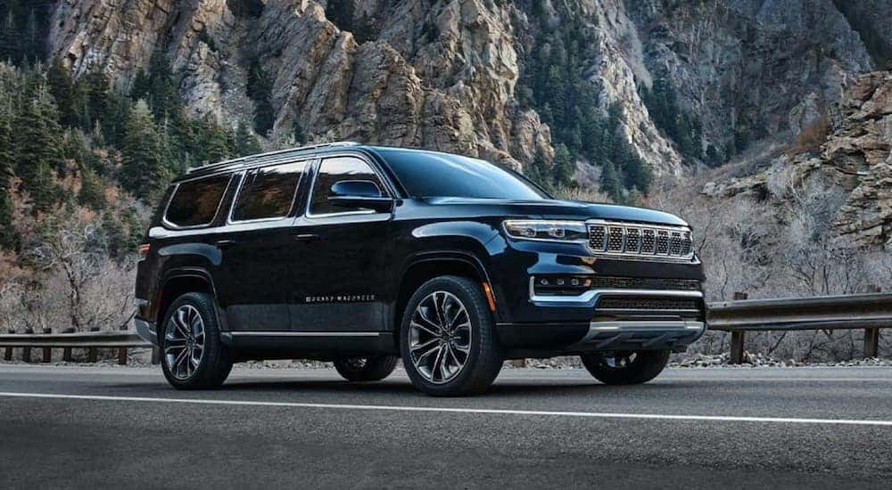 A black 2022 Grand Wagoneer is shown from the side driving on an open road after leaving a Grand Wagoneer dealership.