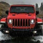 A red 2022 Jeep Wrangler is shown from the front off-roading through a river.