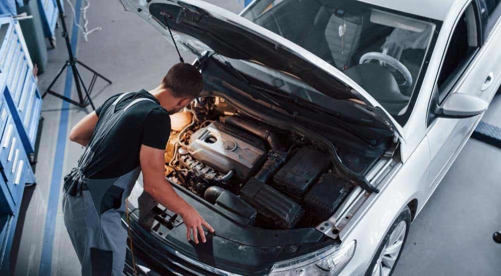 A mechanic is shown inspecting the engine of a vehicle on a used car lot.
