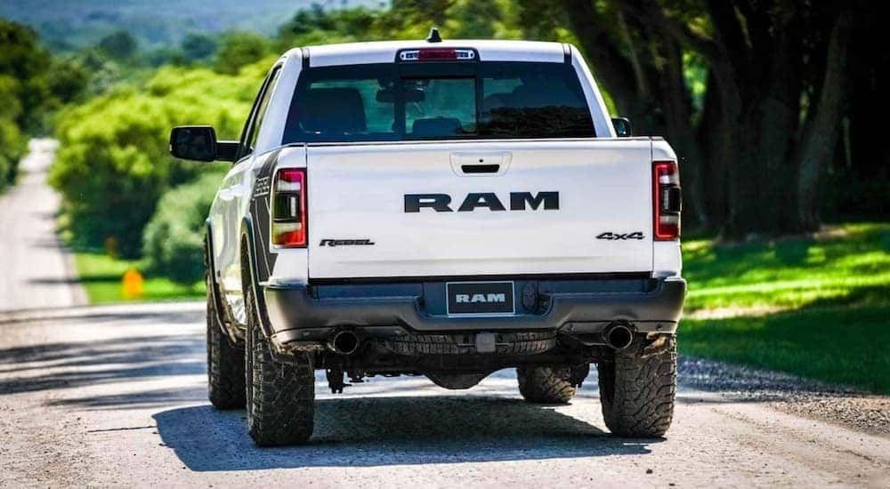 A white 2021 used Ram 1500 Rebel is shown from the rear driving on an open road.