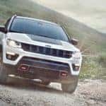 A white 2020 Jeep Compass Trailhawk is shown from the front while it drives down a trail after leaving a certified pre-owned dealer.