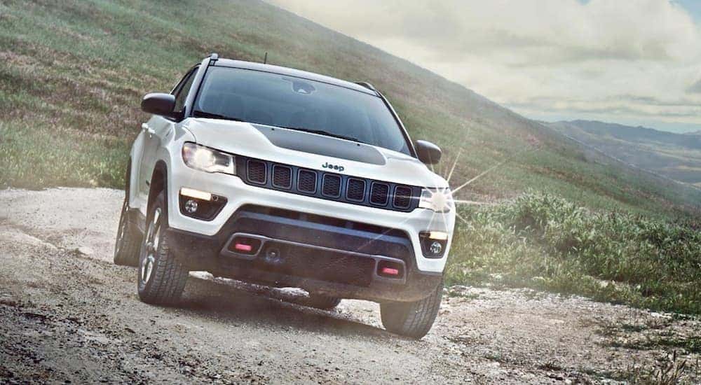 A white 2020 Jeep Compass Trailhawk is shown from the front while it drives down a trail after leaving a certified pre-owned dealer.