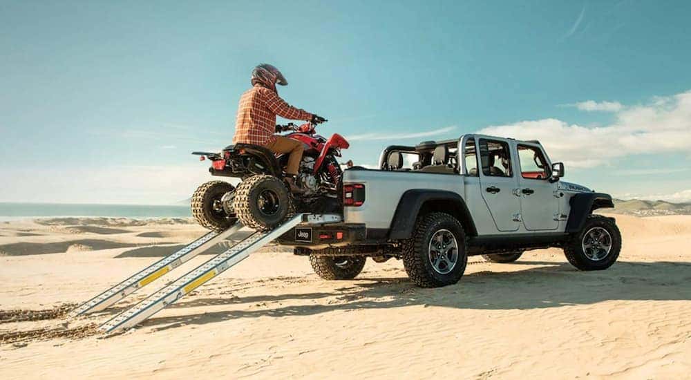 A 2021 Jeep Gladiator Mojave is shown from the rear while parked in the desrt and being loaded with an atv.