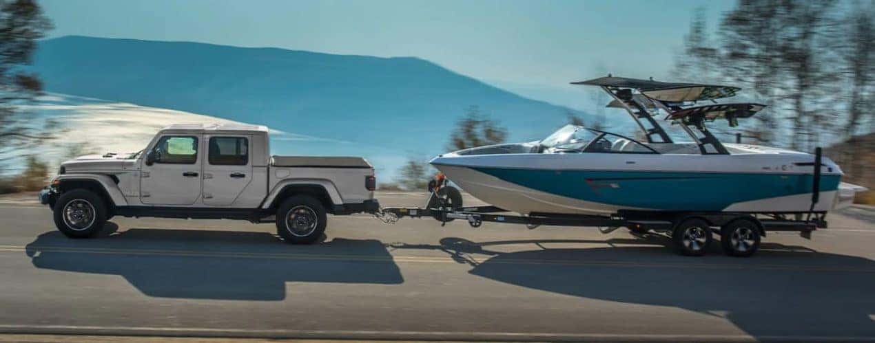 A white 2022 Jeep Gladiator is shown from the side towing a boat on an open road.