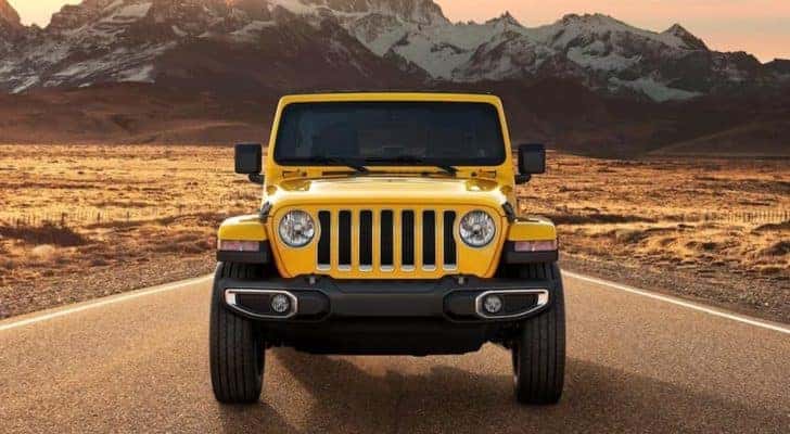 A yellow 2021 Jeep Wrangler is shown from the front driving on an open road.
