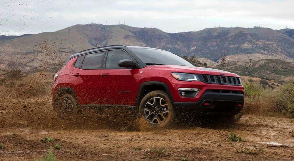 A red 2021 Jeep Compass is shwon from the front at an angle while driving through mud.