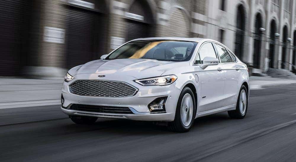 A white 2020 Ford Fusion is shown from the front driving through a city.