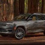 A grey 2022 Jeep Grand Cherokee is shown from the side while parked in the forest after the owner searched 'Grand Cherokee buyers guide'.