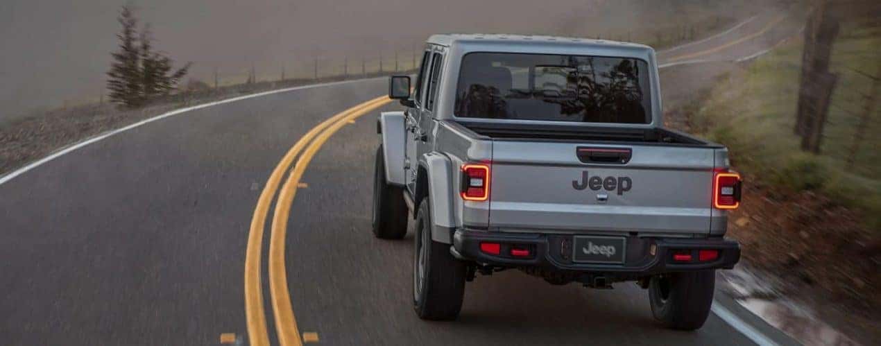 A silver 2022 Jeep Gladiator is shown from the rear driving on a foggy road.