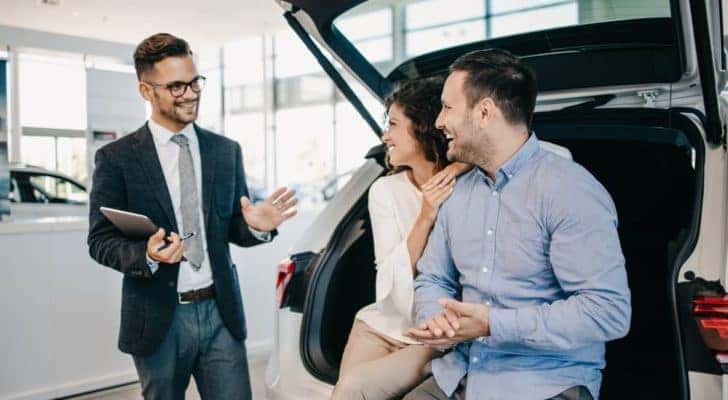 A salesman is shown speaking to customers at an affordable used car dealer.