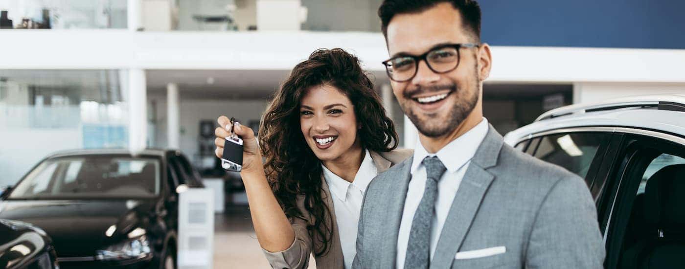 A salesperson is shown next to a customer holding a car key.