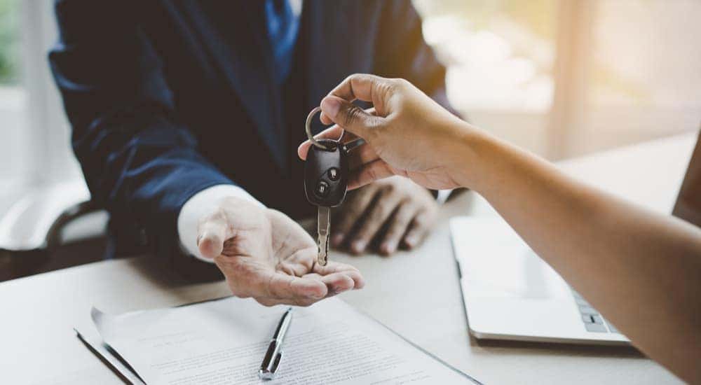 A customer is shown handing a car key to a salesman.