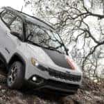 A white 2022 Jeep Compass Trailhawk is shown off-roading on a steep rocky trail.