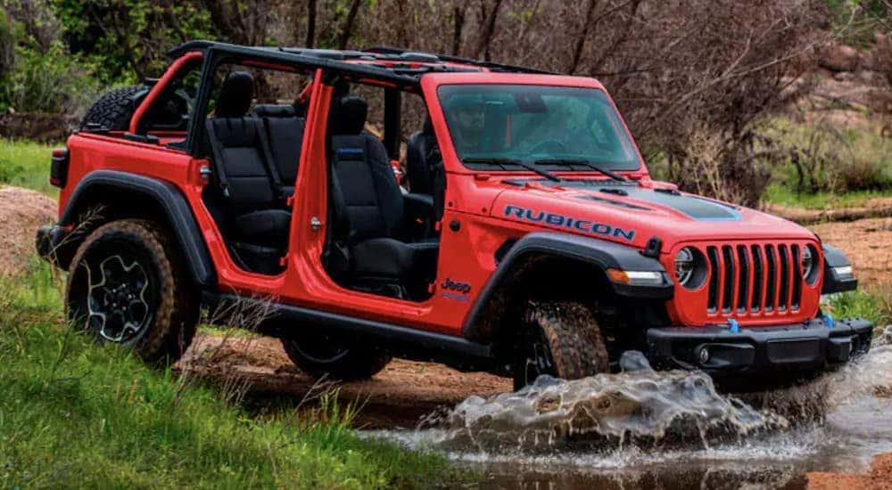 A red 2022 Jeep Wrangler 4xe is shown off-roading through a stream.