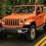 An orange 2020 Jeep Wrangler is shown from the front driving on an open road.