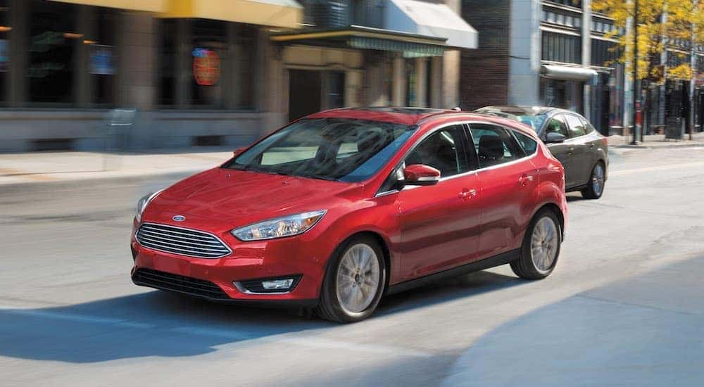 A red 2016 Ford Focus is shown from the side driving through a city after looking at cheap cars for sale.