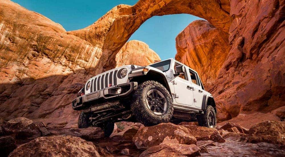 A white 2020 Jeep Wrangler is shown off-roading on a trail after viewing cheap used cars for sale.