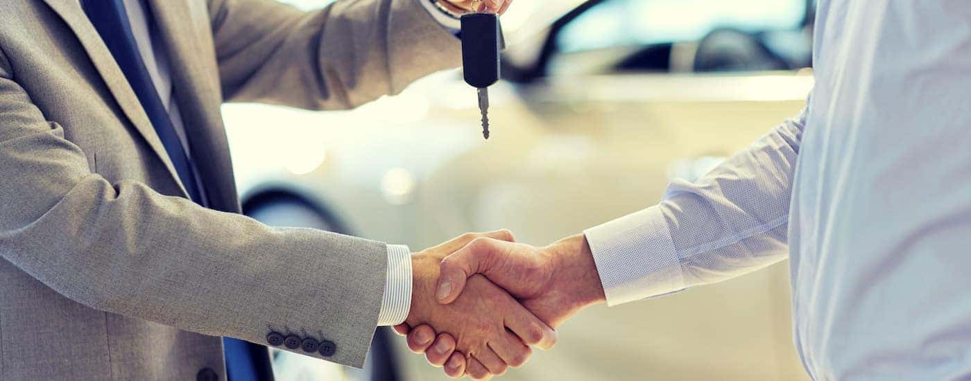 A salesperson is shown passing a key at a used car lot.