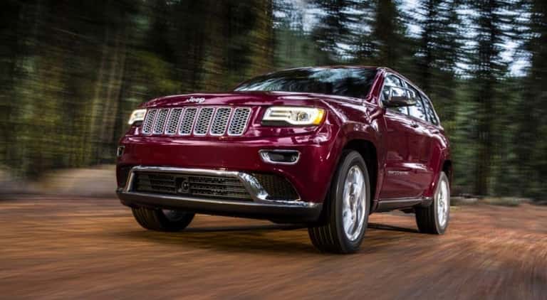 A maroon 2016 Jeep Grand Cherokee is shown from the front driving through the woods.