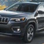 A grey 2021 Jeep Cherokee is shown from the front driving on an open road.