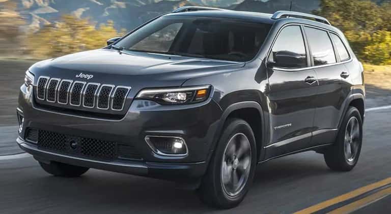 A grey 2021 Jeep Cherokee is shown from the front driving on an open road.