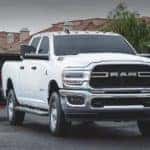 A white 2020 Ram 2500 is shown from the front towing heavy machinery.