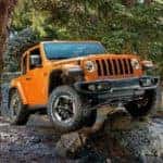 An orange 2019 Jeep Wrangler is shown from the front while driving over a rock after leaving a dealership that advertises used Jeep Wrangler for sale.