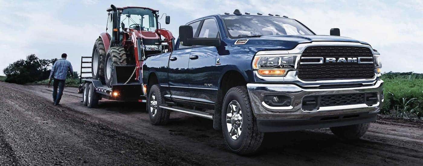 A blue 2022 Ram 2500 is shown towing a tractor on a dirt road.