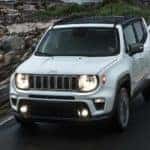 A popular used SUV for Sale, a white 2020 Jeep Renegade, is shown driving on a highway.