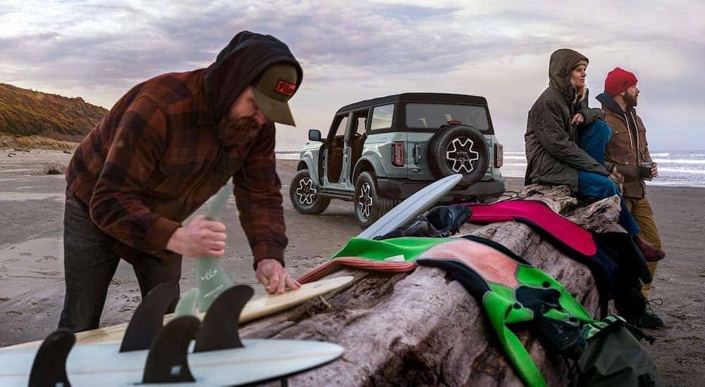 A light blue 2021 Ford Bronco Outer Banks is shown on the beach near surfers.