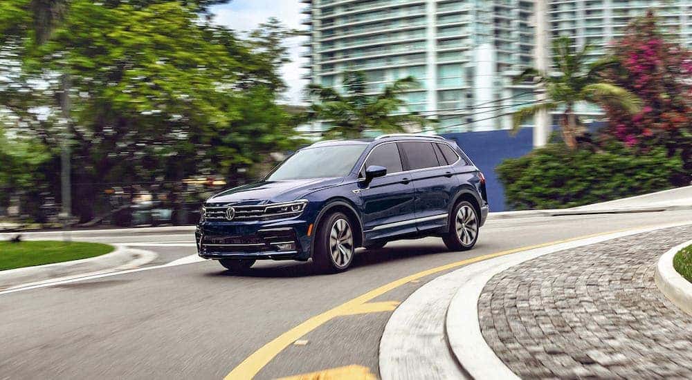 A dark blue 2021 Volkswagen Tiguan is shown driving on a city street.
